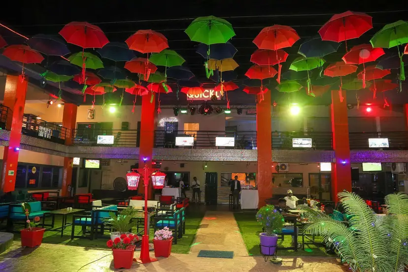 La cour de Quickly la nuit : des parapluies rouges et verts suspendus au-dessus des tables, éclairés par des néons.