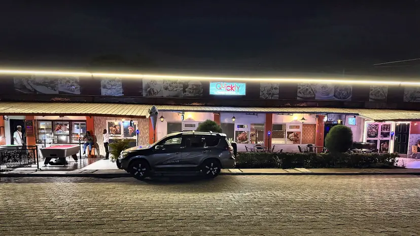 La façade de Quickly le soir : l’enseigne lumineuse, la terrasse éclairée et une table de billard sous l’auvent.