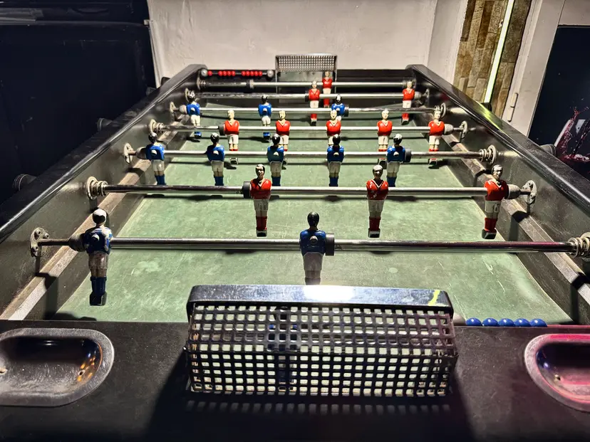 Un baby-foot vu depuis le but, joueurs rouges et bleus alignés.