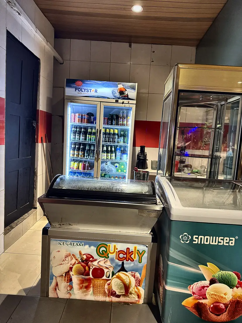 Le coin glaces : un bac à glaces décoré « Ice cream Quickly » devant un frigo de boissons.