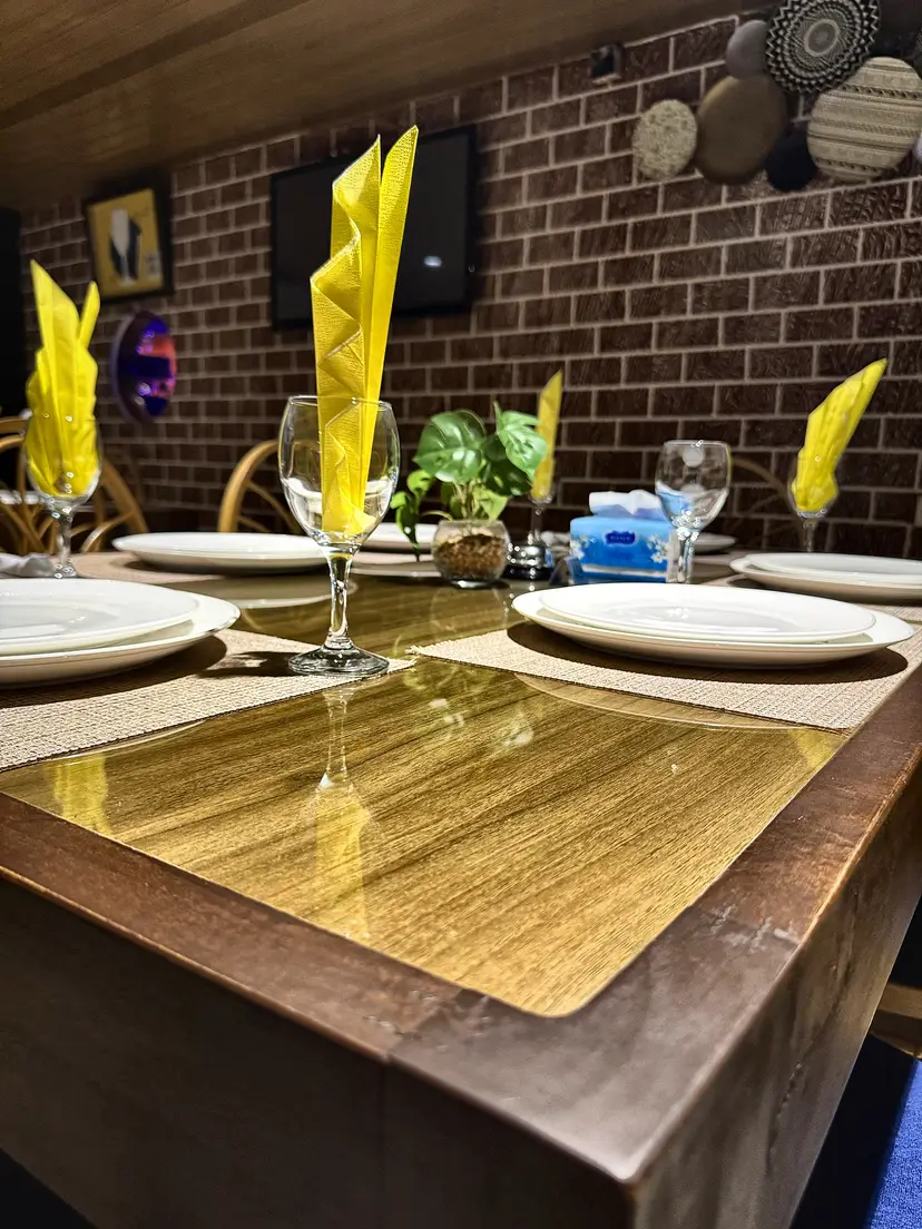 Une table dressée devant le mur de briques : verres à pied, serviettes jaunes et petite plante.