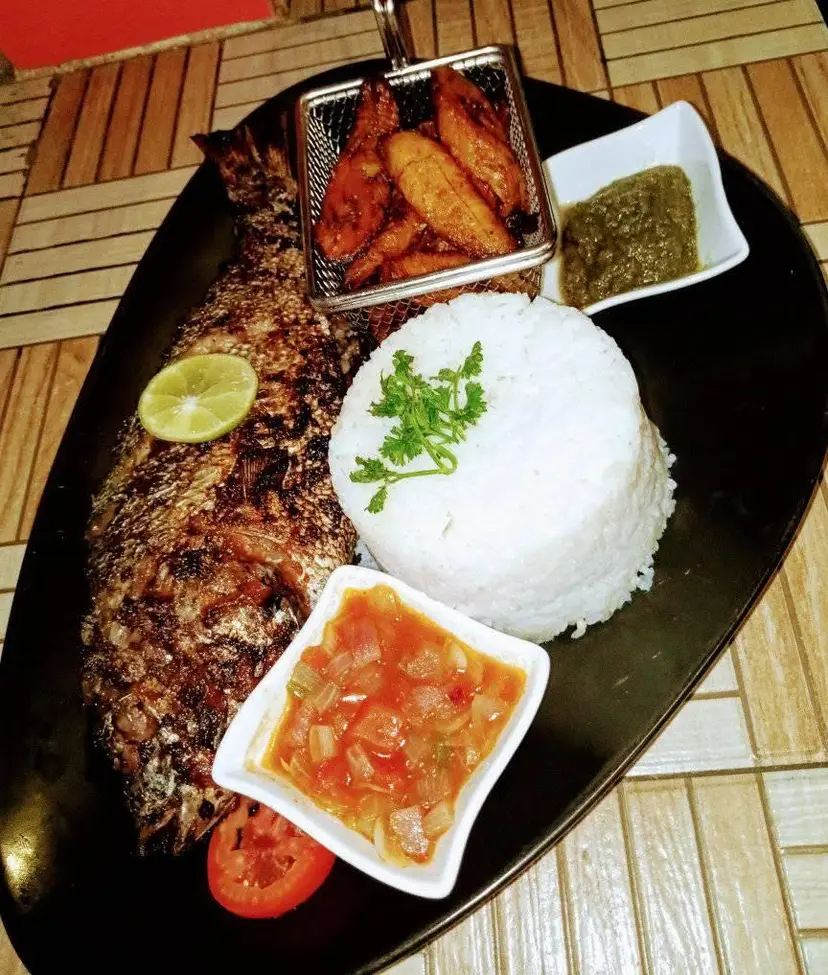 Un poisson braisé servi avec du riz blanc, des crudités et une sauce rouge.